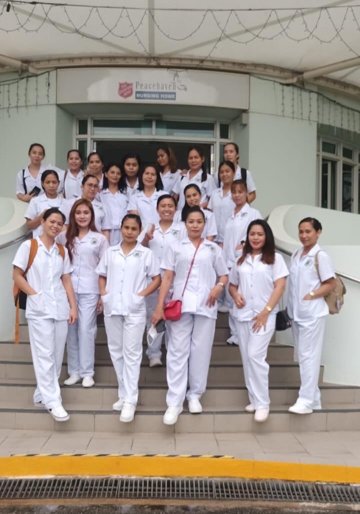 A group of female students in white uniforms posing for a photo in front of Peacehaven Nursing Home